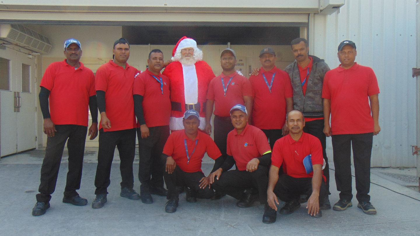 KBR’s Isa Air Base galley staff pose outside in preparation of their annual holiday dinner alongside Santa Claus, who visited to help cut the cake and spread Christmas cheer to patrons.